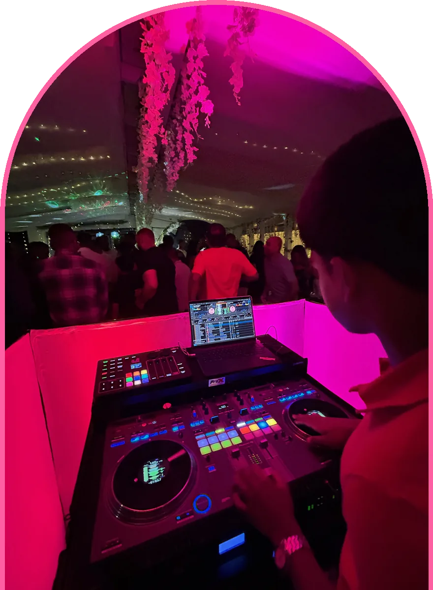 DJ Syid mixing at a tent party under pink lights, crowd dancing behind him