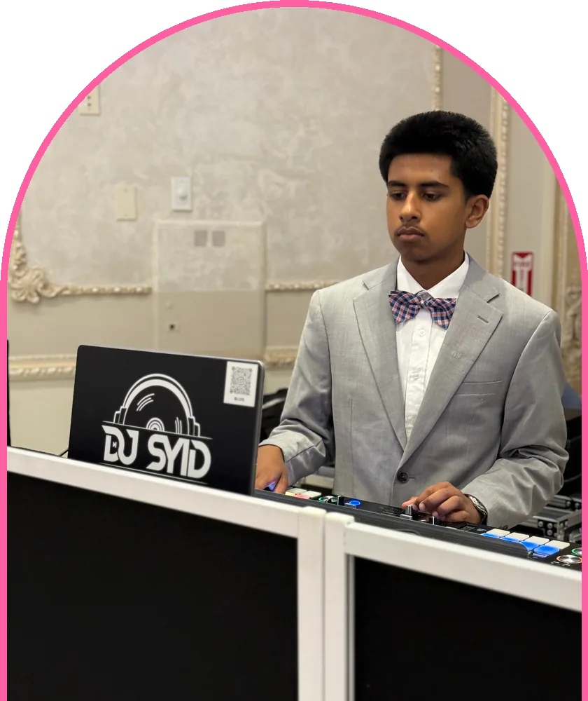 DJ Syid in a grey suit and bow tie at his DJ booth